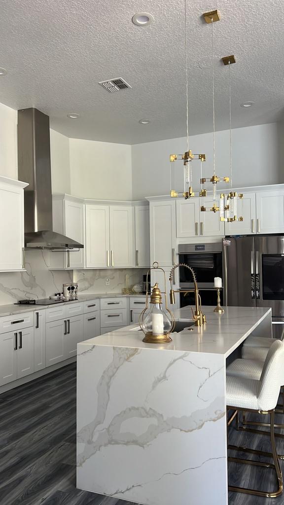 White kitchen island with a marble waterfall countertop and gold pendant lighting